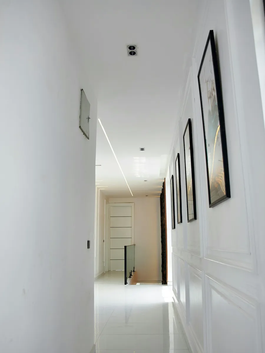 Couloir aux murs blancs lisses, cadres alignés et sol clair